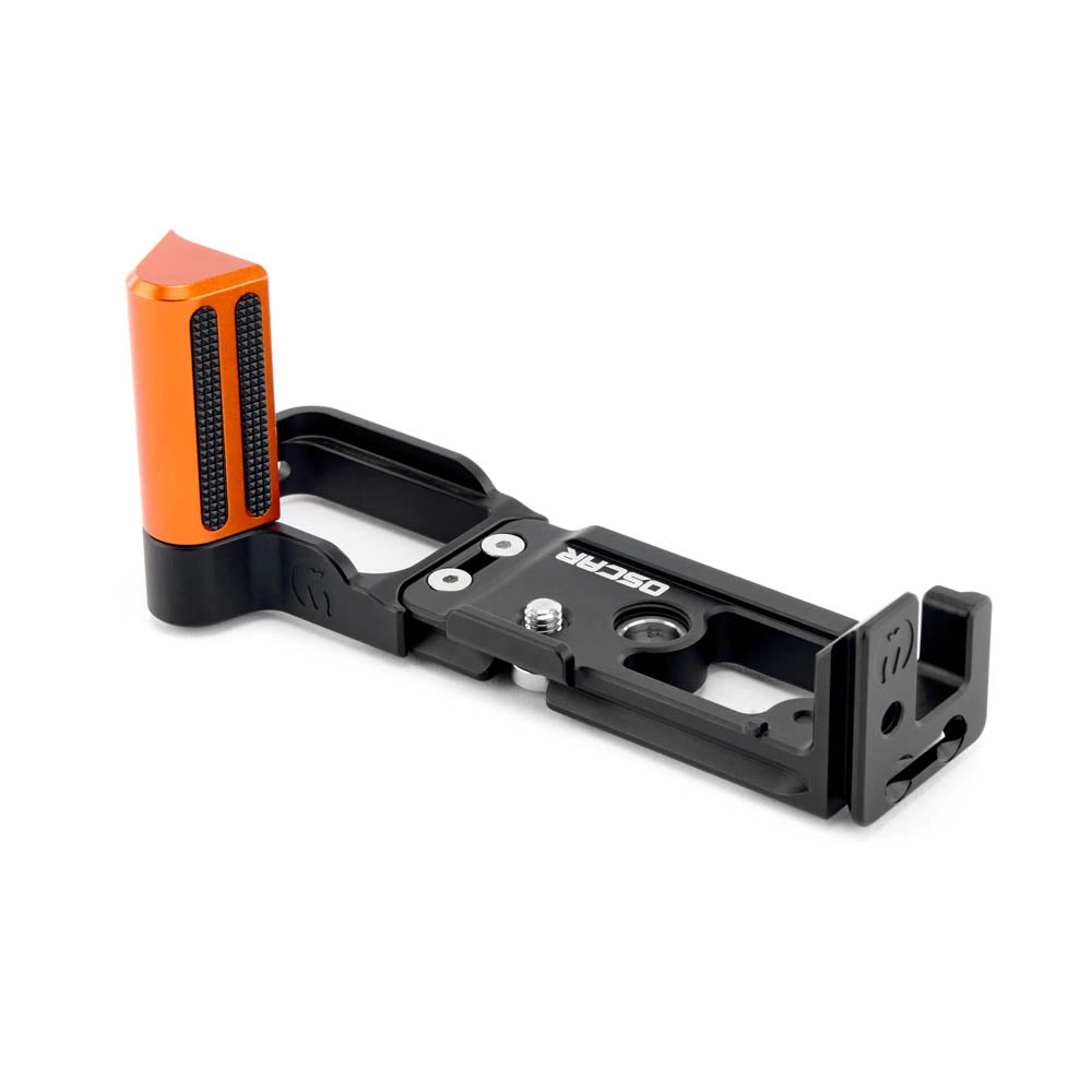 A black metal camera grip extension with an orange textured handle grip, featuring the brand name 'OSCAR' printed on the side, set against a plain white background.
