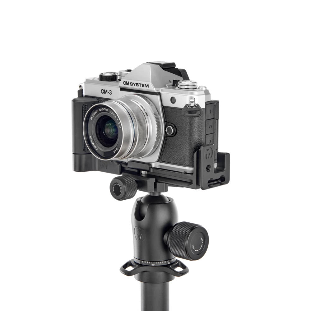 A silver and black OM System OM-3 mirrorless camera mounted on a black camera rig with a ball head, shown against a solid white background.