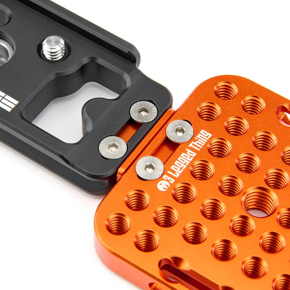Close-up of a black and orange metal camera mounting bracket with threaded holes and silver screws, on a white background. The orange section has '3 Legged Thing' printed on it.