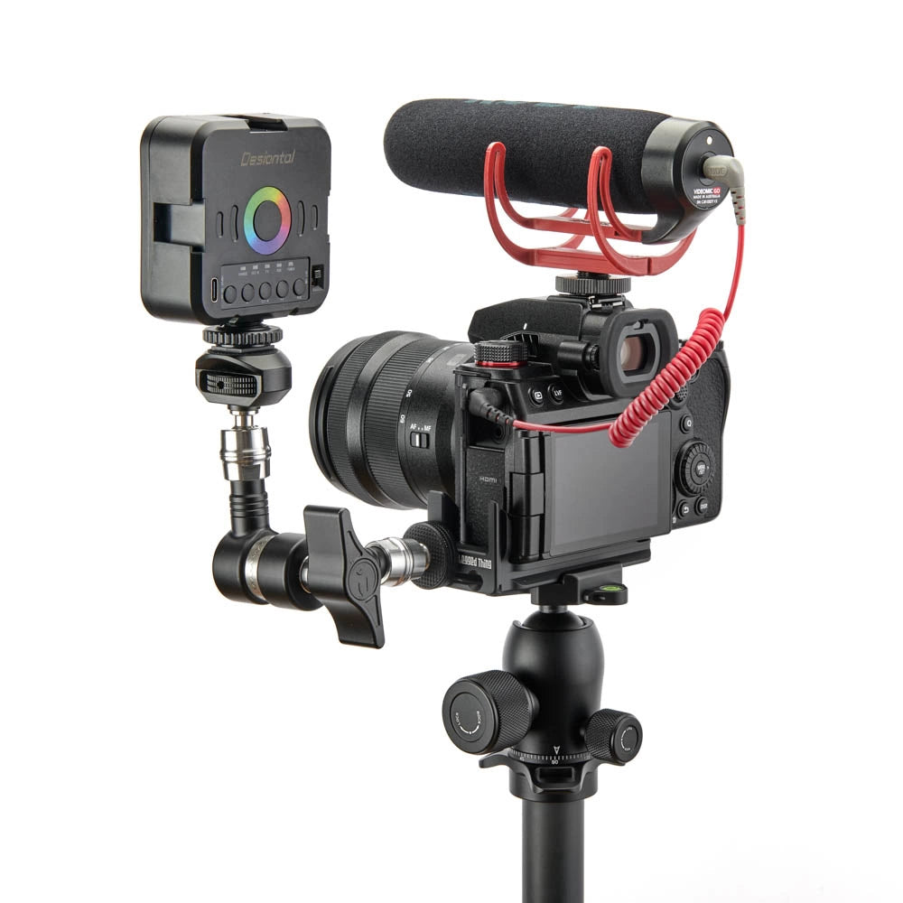 A camera rig setup featuring a Lumix camera with a lens, a red microphone stand, a shotgun microphone, a wireless transmitter, and a monitor screen, all mounted on a tripod against a white background.