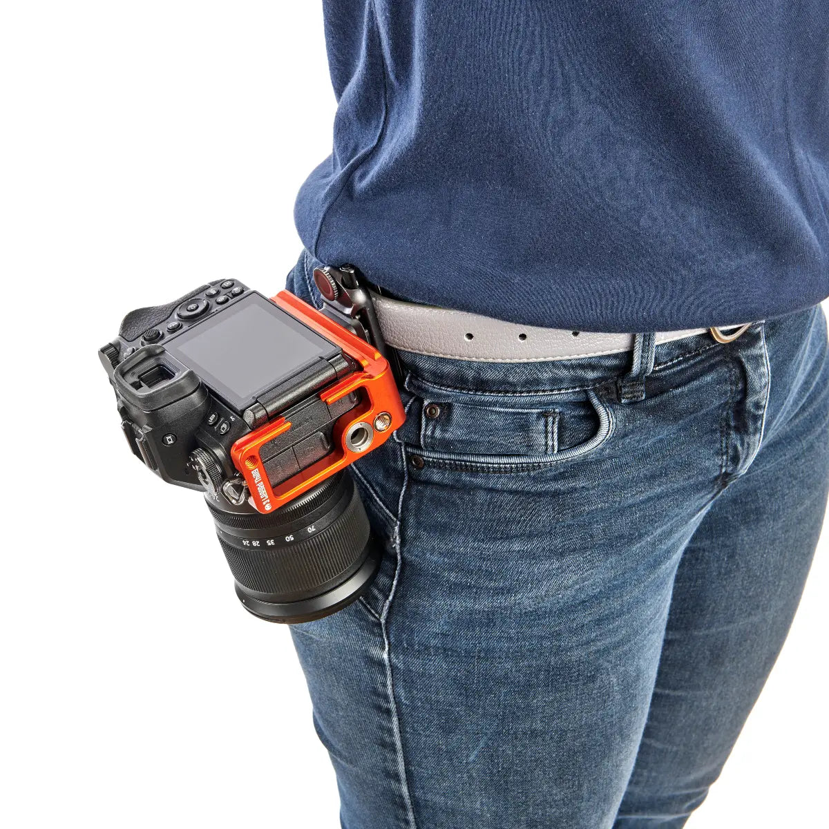 Camera with an orange and black holder attached to a person wearing blue jeans and a navy shirt.