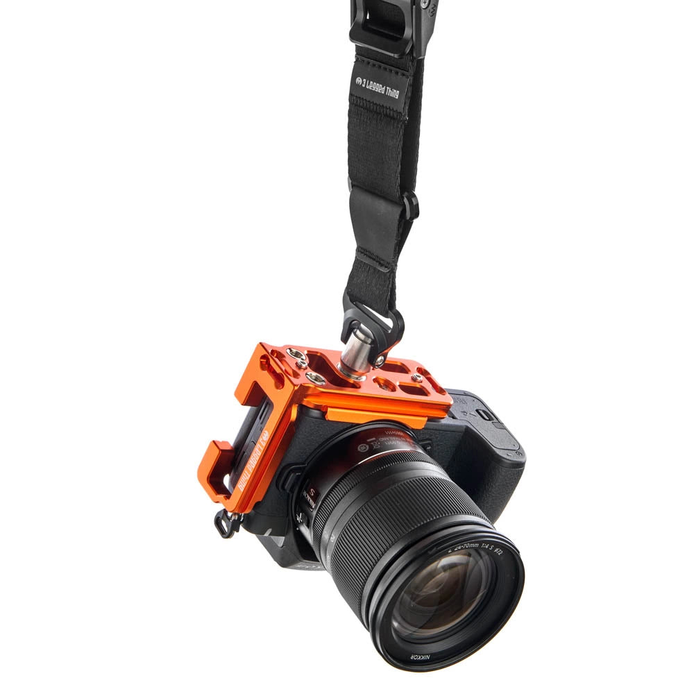 An orange camera rig mount holding a black Nikon camera with a lens, suspended by a black strap against a plain white background.