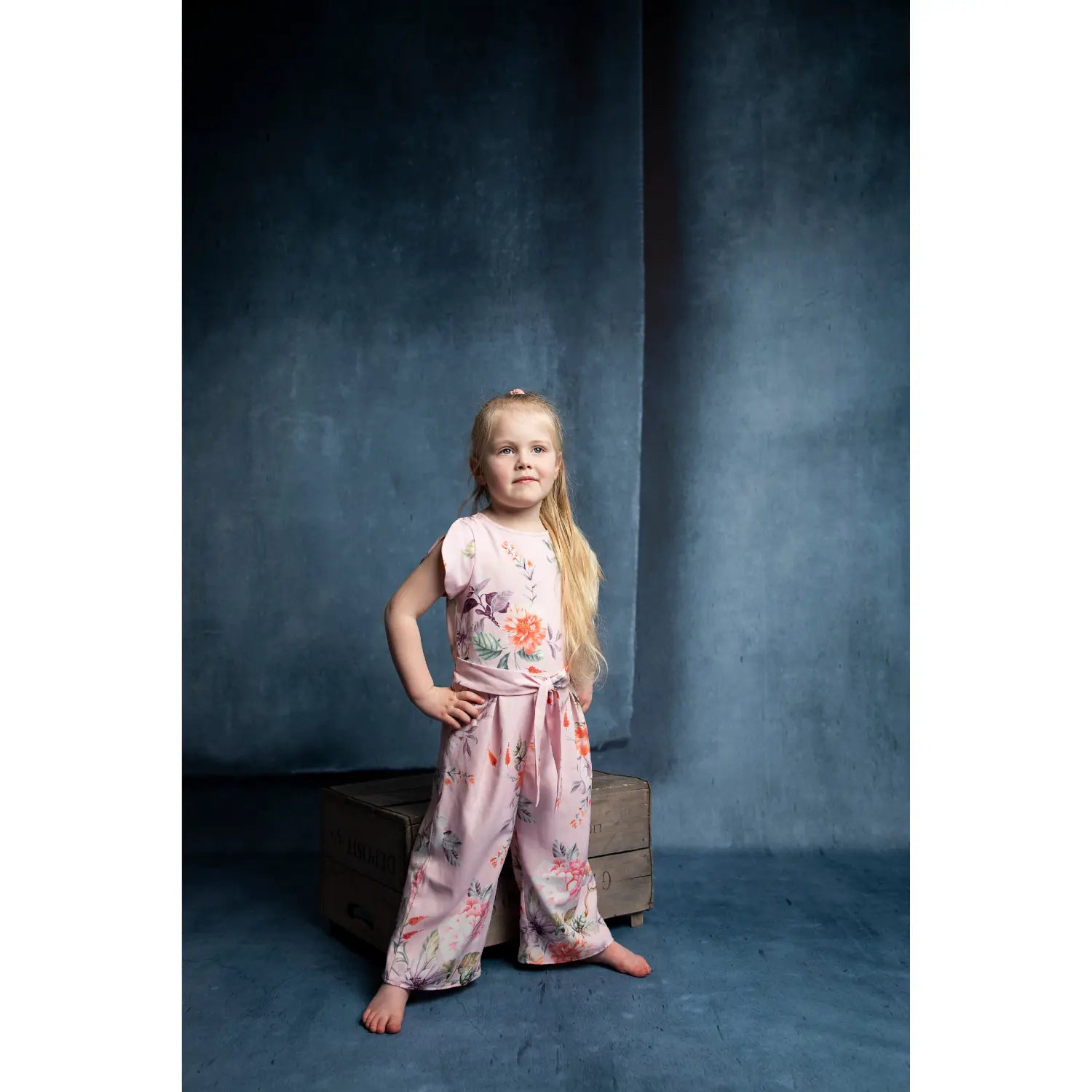 Young girl in a floral outfit standing against a dark blue background