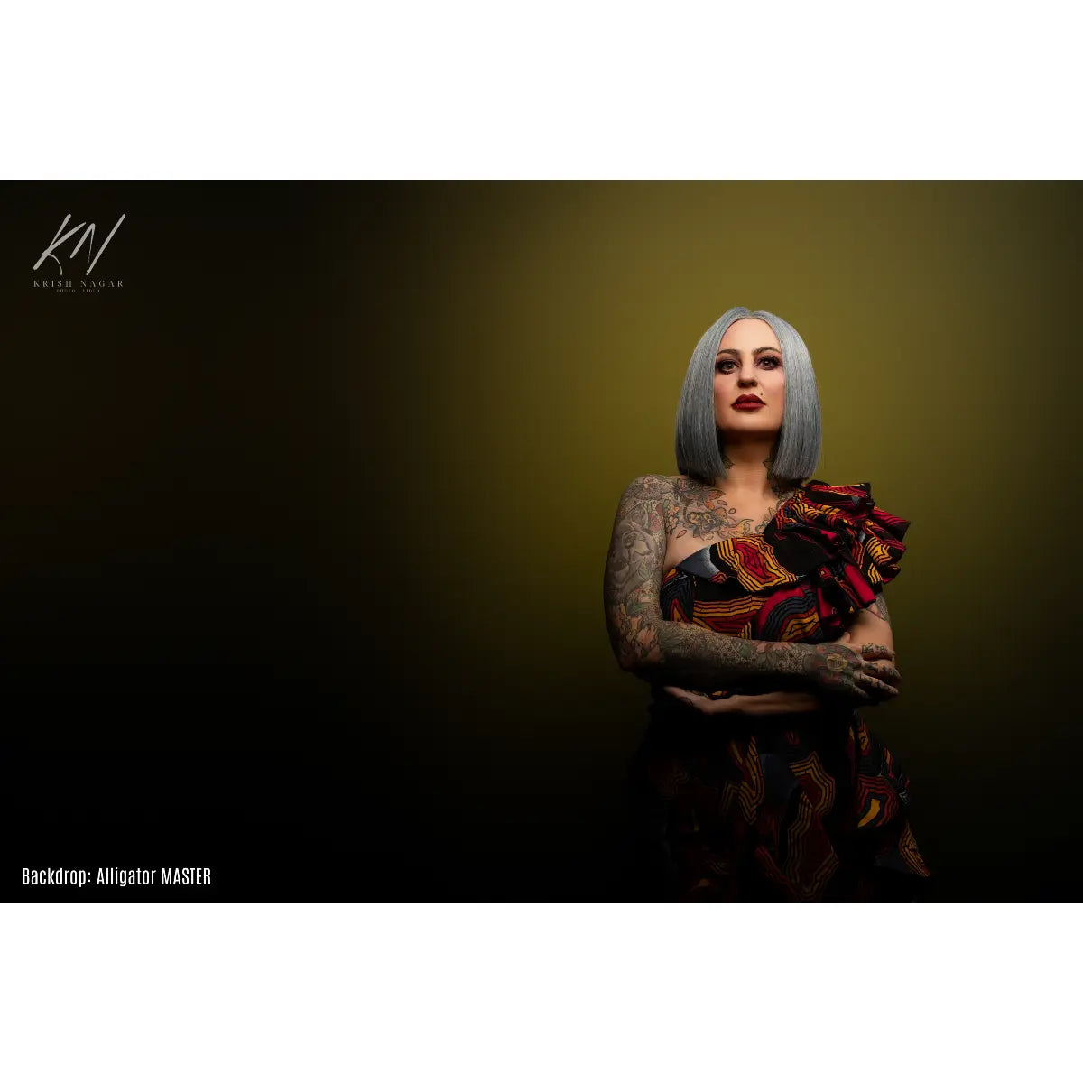 Woman with tattoos and gray hair wearing a colorful dress against a dark background