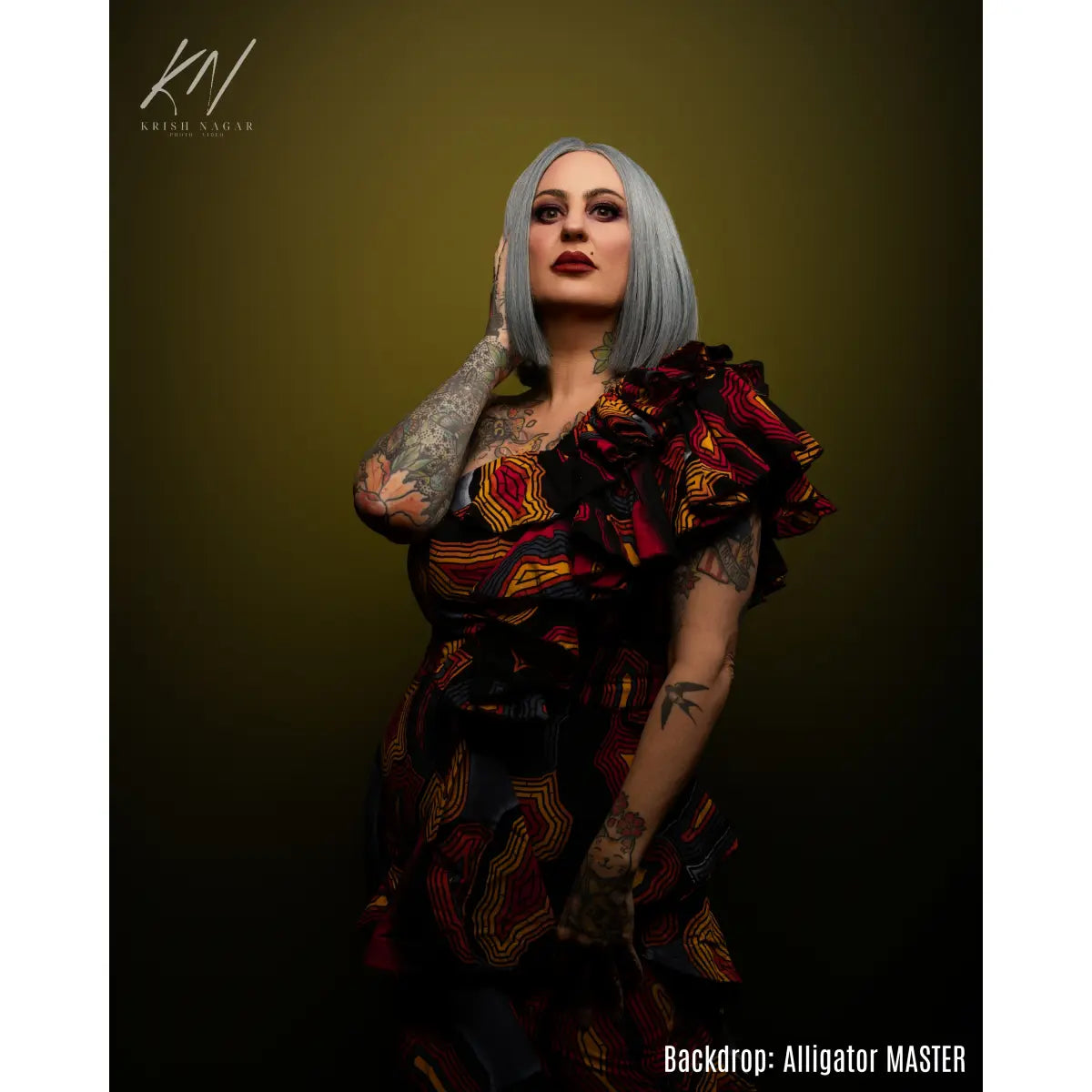 Person with tattoos and a colorful dress against a dark background