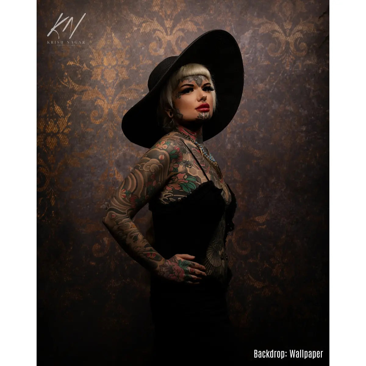 Person with tattoos wearing a black hat against an ornate wallpaper backdrop