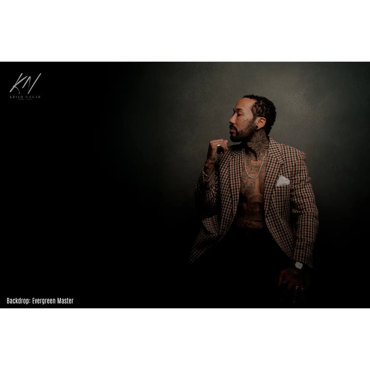 Man in a checkered suit with a tattooed arm against a dark background