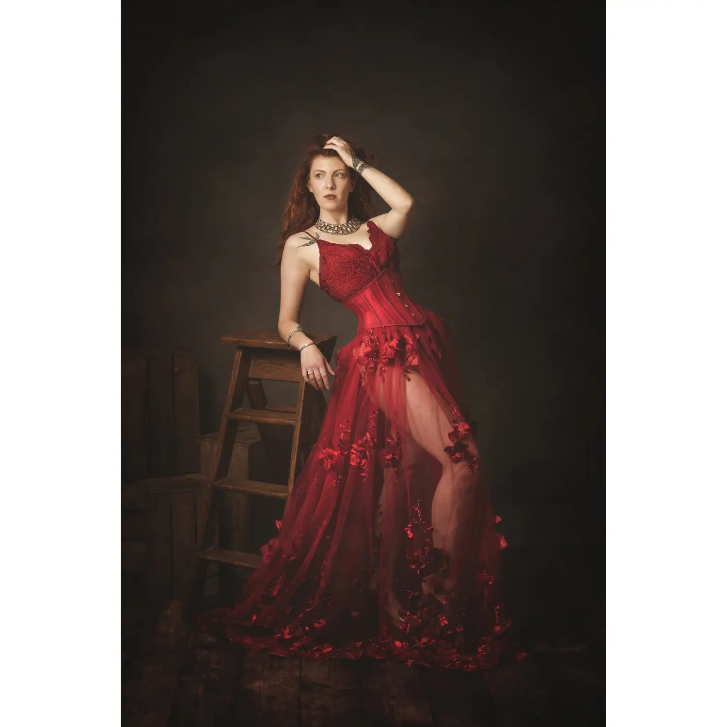 Woman in a red dress standing on a wooden ladder against a dark background