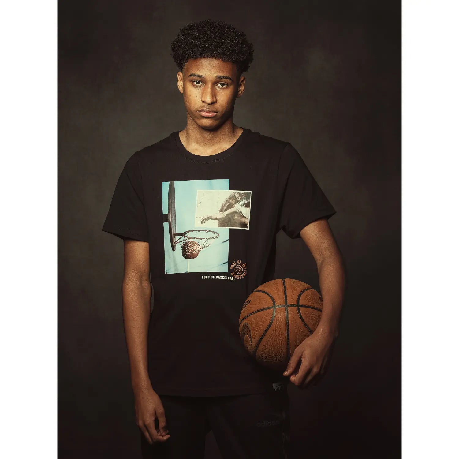 Person wearing a black t-shirt with a graphic design holding a basketball against a dark background