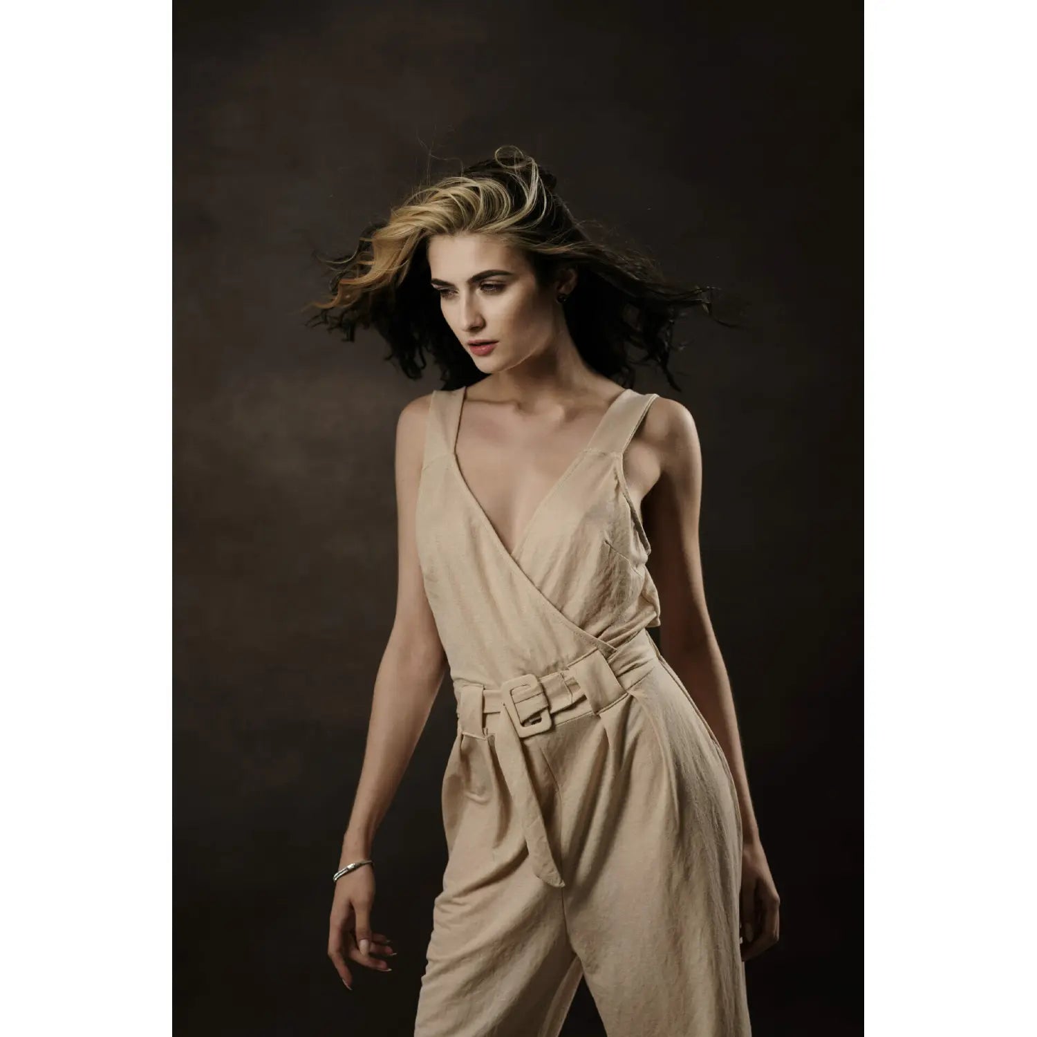 Woman wearing a beige sleeveless jumpsuit against a dark background