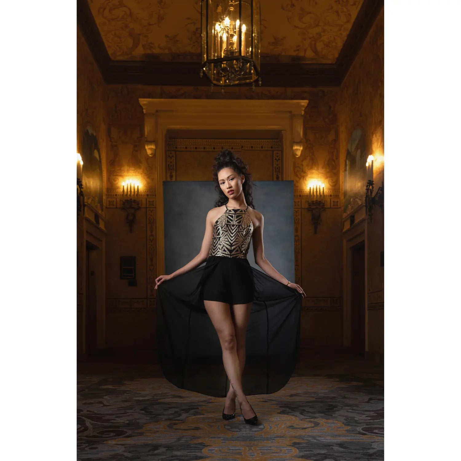 Woman in a black dress posing in an elegant room with chandelier