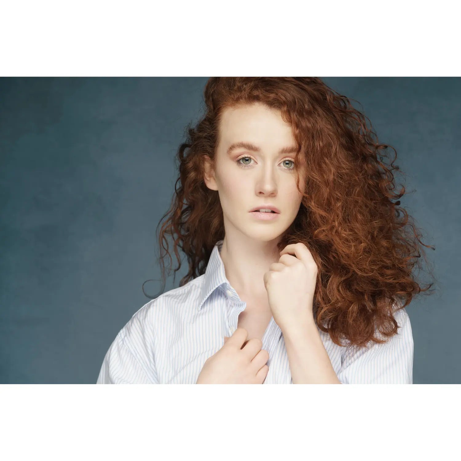 Woman with curly hair wearing a white shirt against a blue background