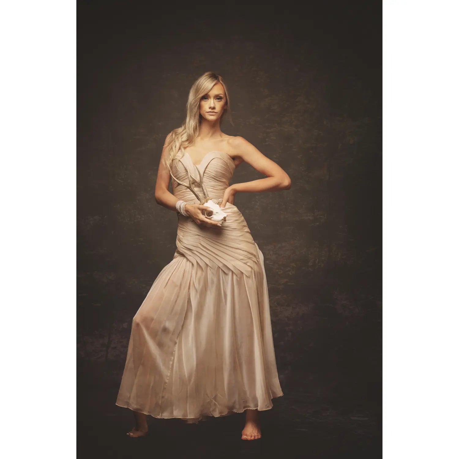 Woman in a beige strapless gown holding a small object against a dark background