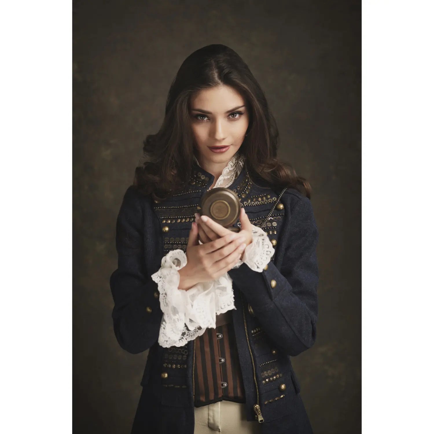 Woman in a dark, ornate outfit holding a small round object against a dark background