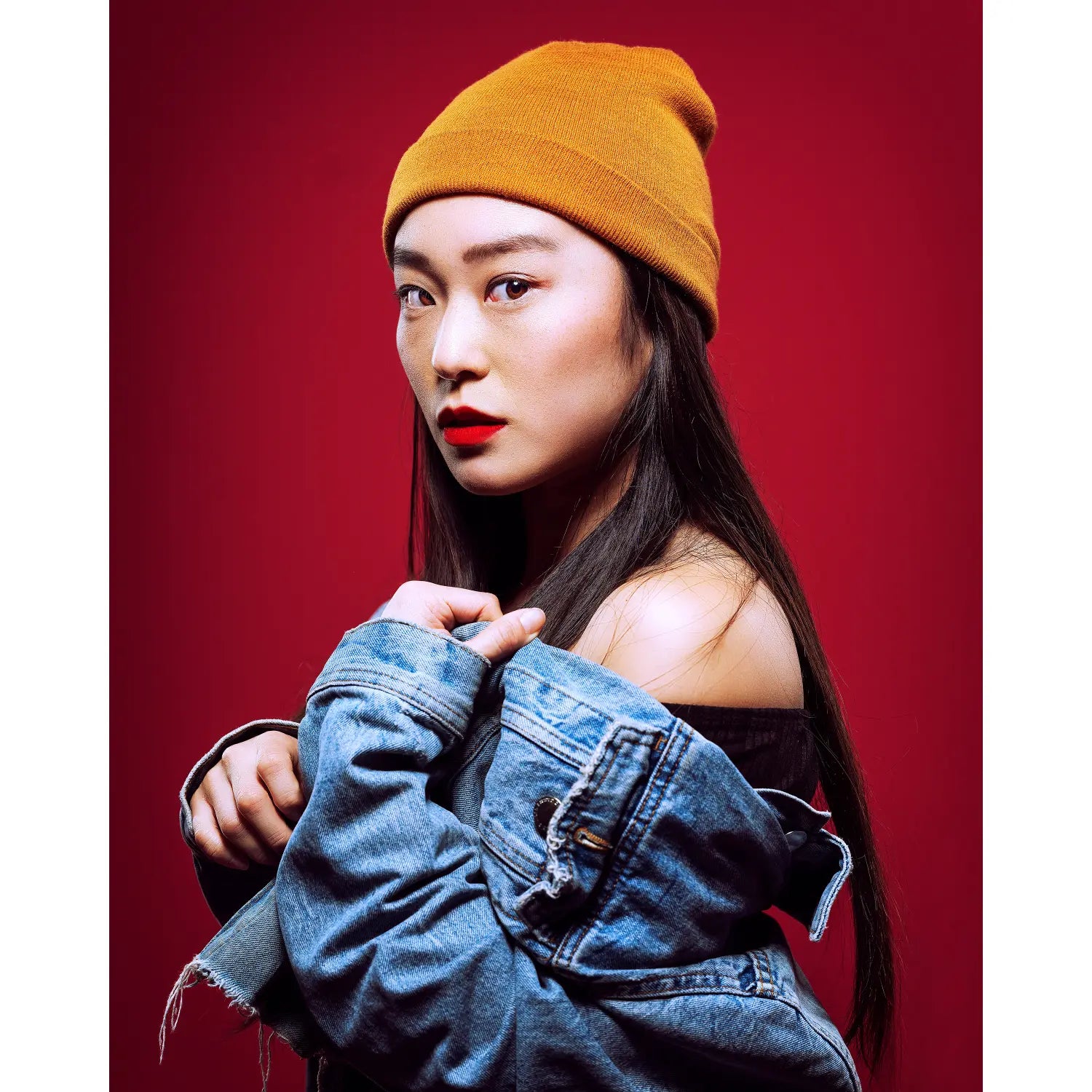 Woman wearing a yellow beanie and blue denim jacket against a red background