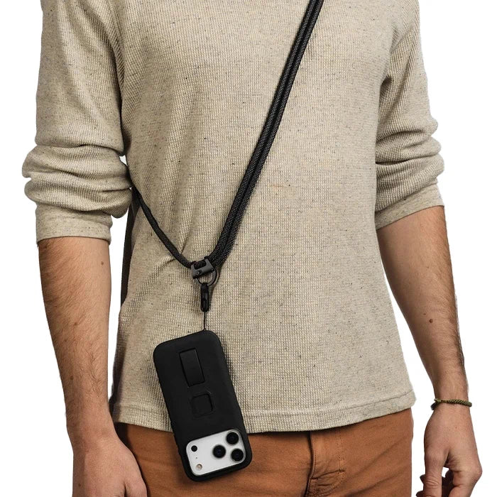 A person wearing a beige ribbed long-sleeve shirt and brown pants, shown from the chest down, wearing a black phone strap with a black phone case hanging from it.