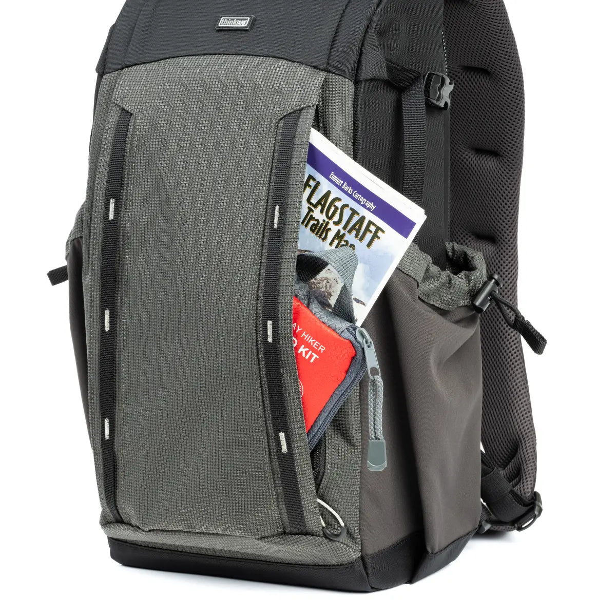 Gray backpack with a magazine and red item sticking out of a pocket on a white background