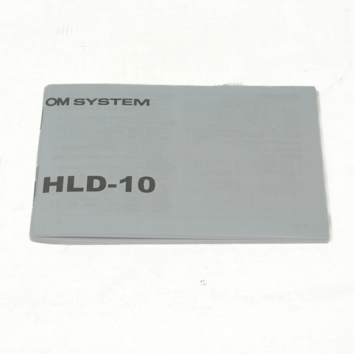 Gray rectangular object with 'OM SYSTEM' and 'HLD-10' text on a white background