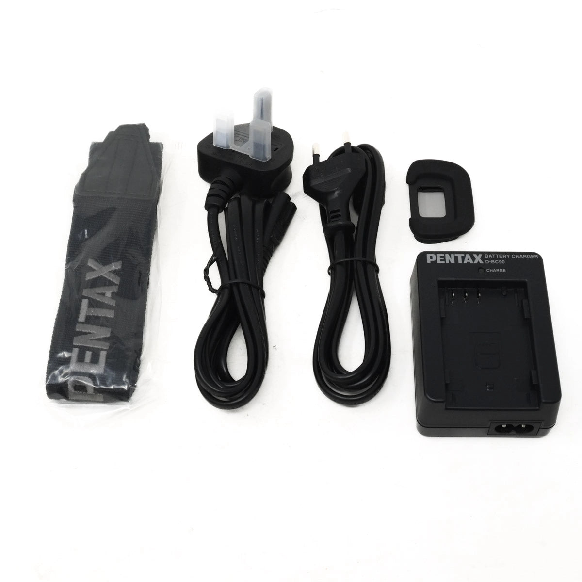 Pentax camera accessories including a battery charger, cables, eyecup and strap on a white background
