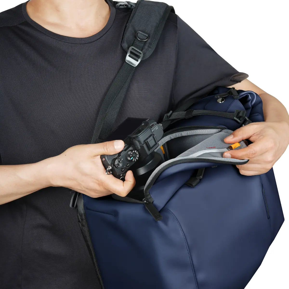 Person holding a blue duffel bag with a camera and other items, wearing a black shirt.