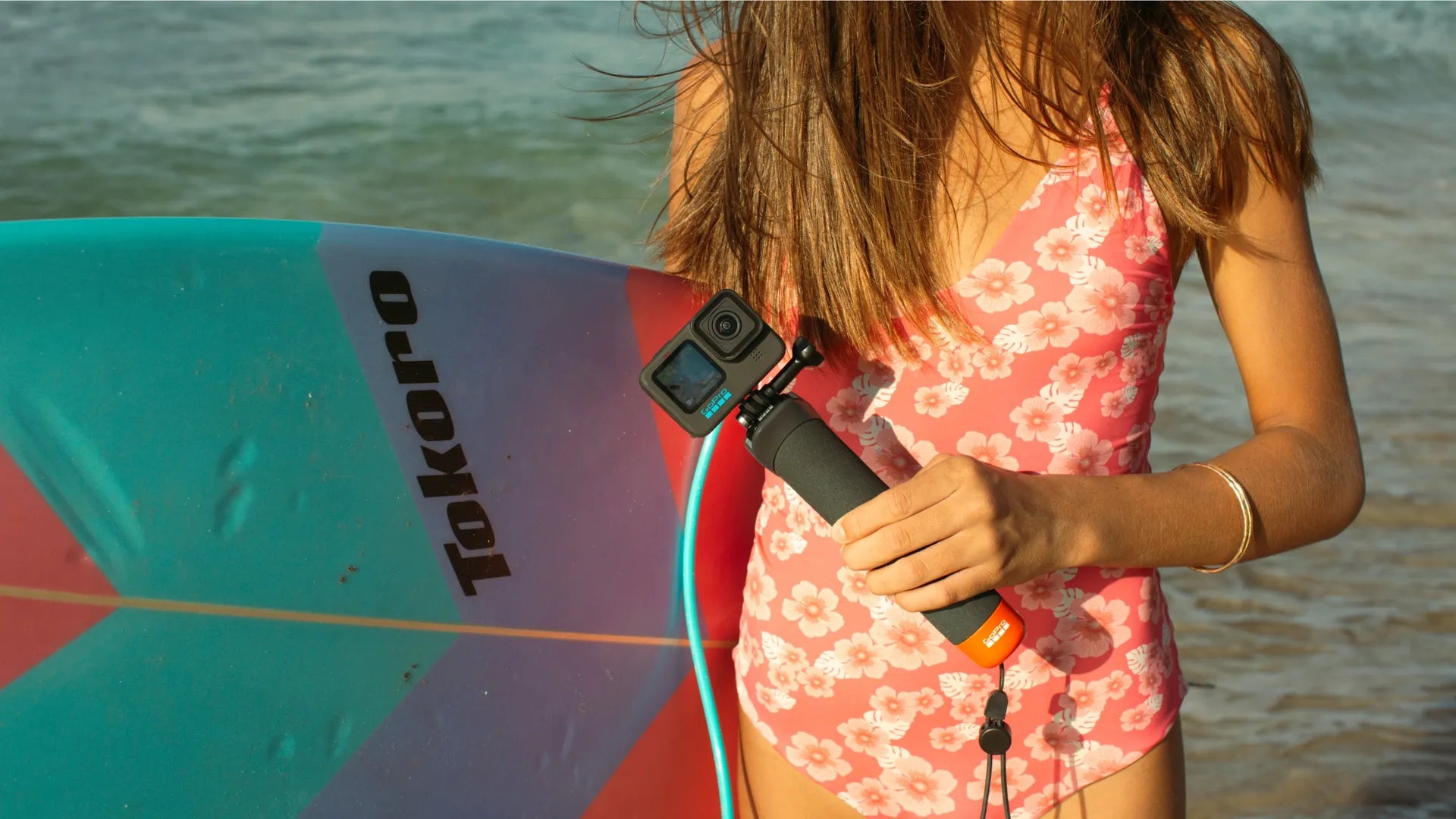 Lifestyle shot of a female surfer about to go surfing whilst holding the gopro grip