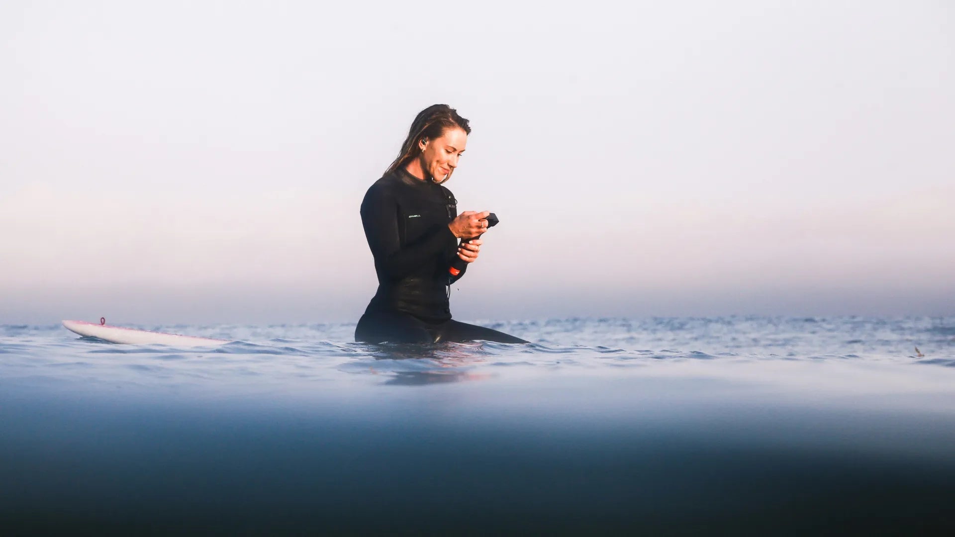 Lifestyle shot of a female surfer chilling in the water reviewing footage with a gorgeous misty background
