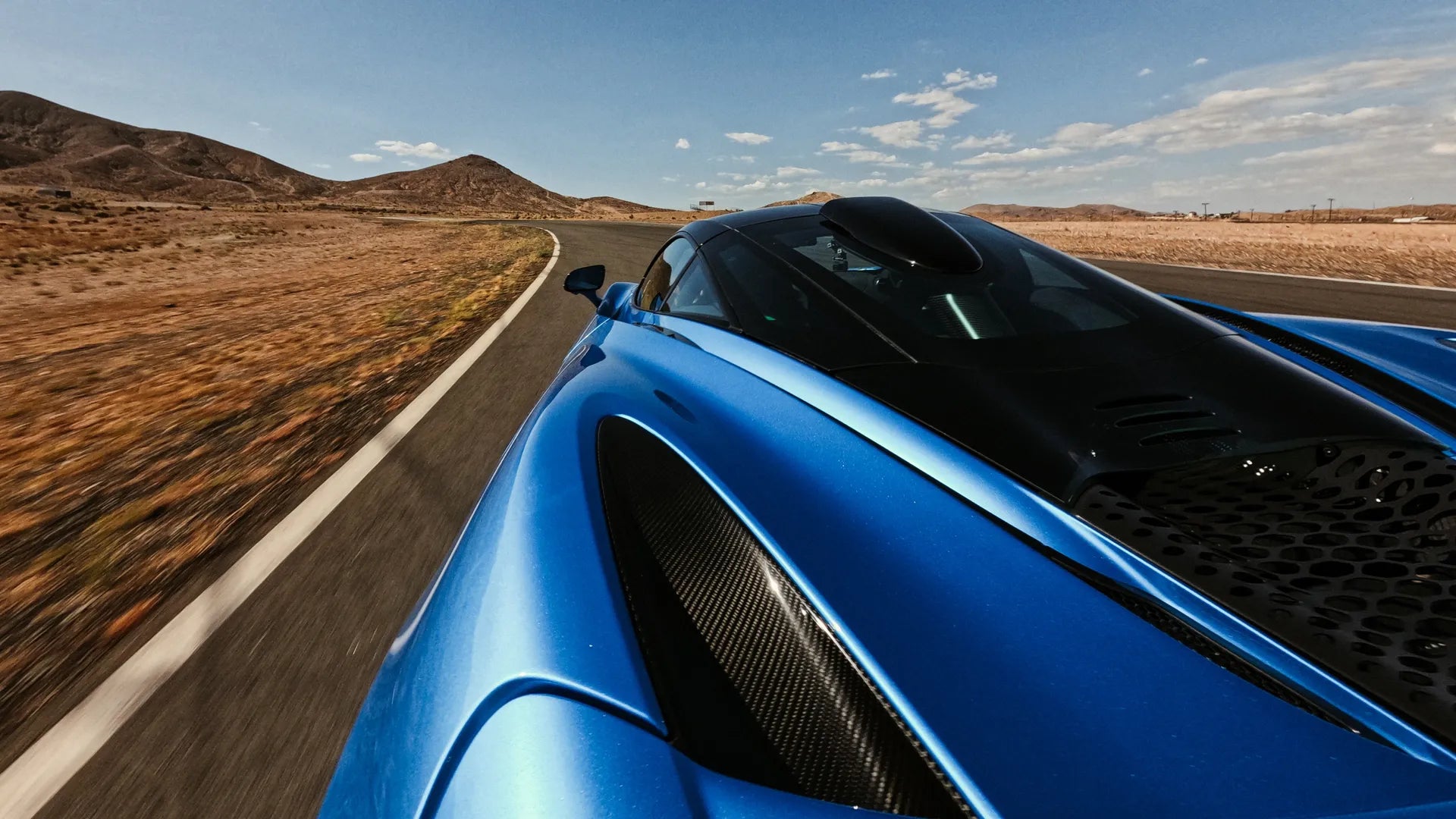 Lifestyle shot - Blue super car driving in the sunny desert with the mount attached to the rear of the car