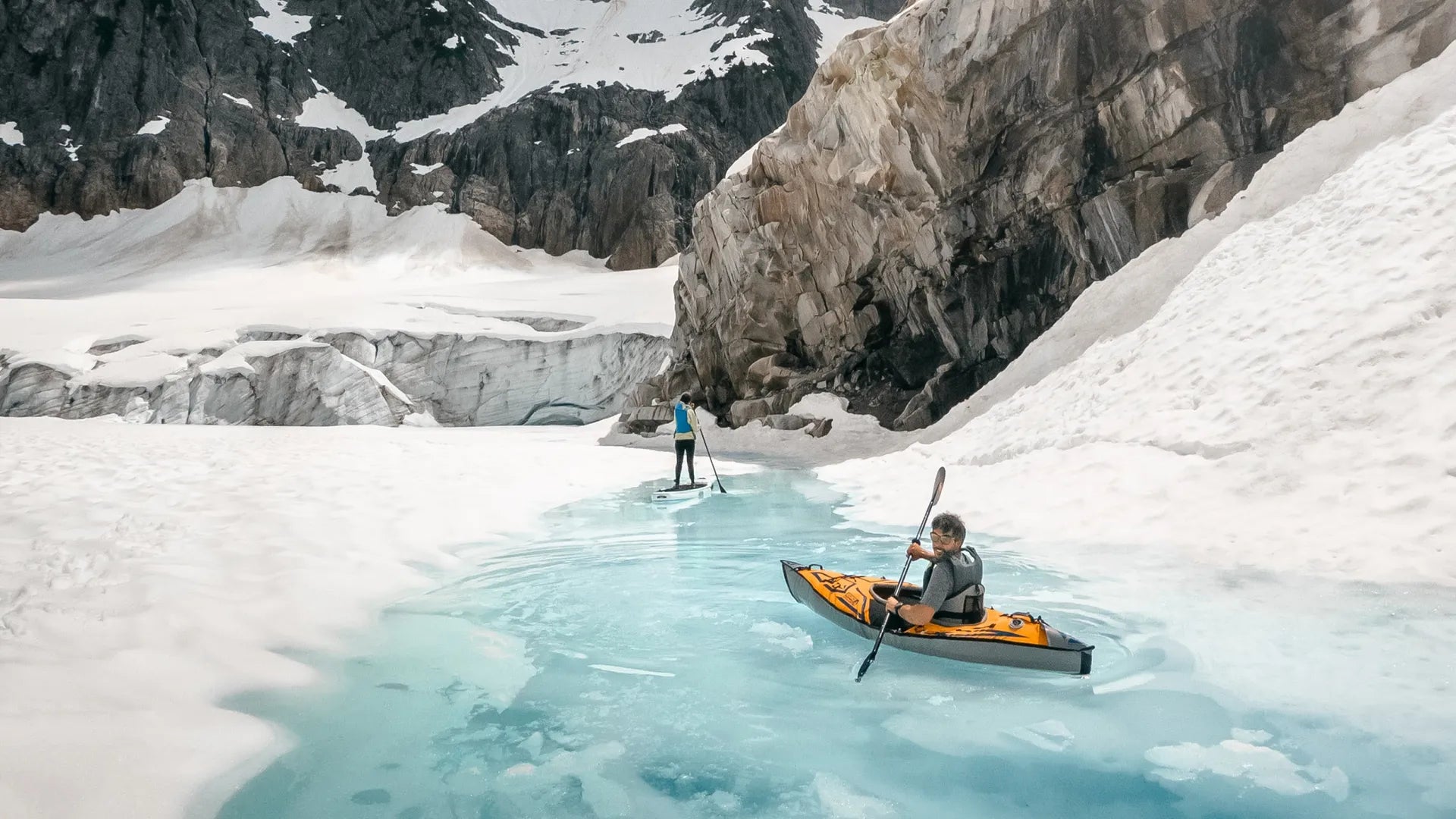 Lifestyle photo of a kayaker and paddlevboarder paddling through an icy river in the snowy mountains