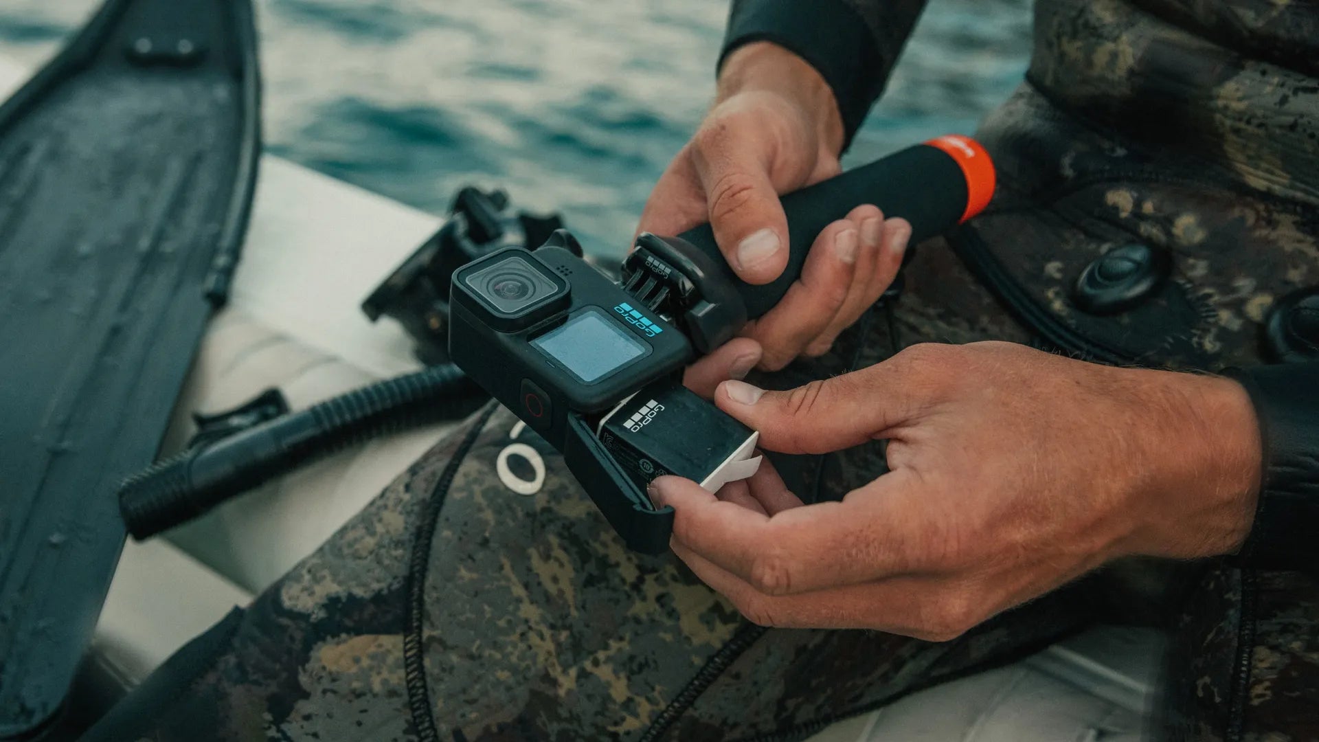 Lifestyle photo of a diver adding the battery to the camera attached to a grip whilst sitting in a boat