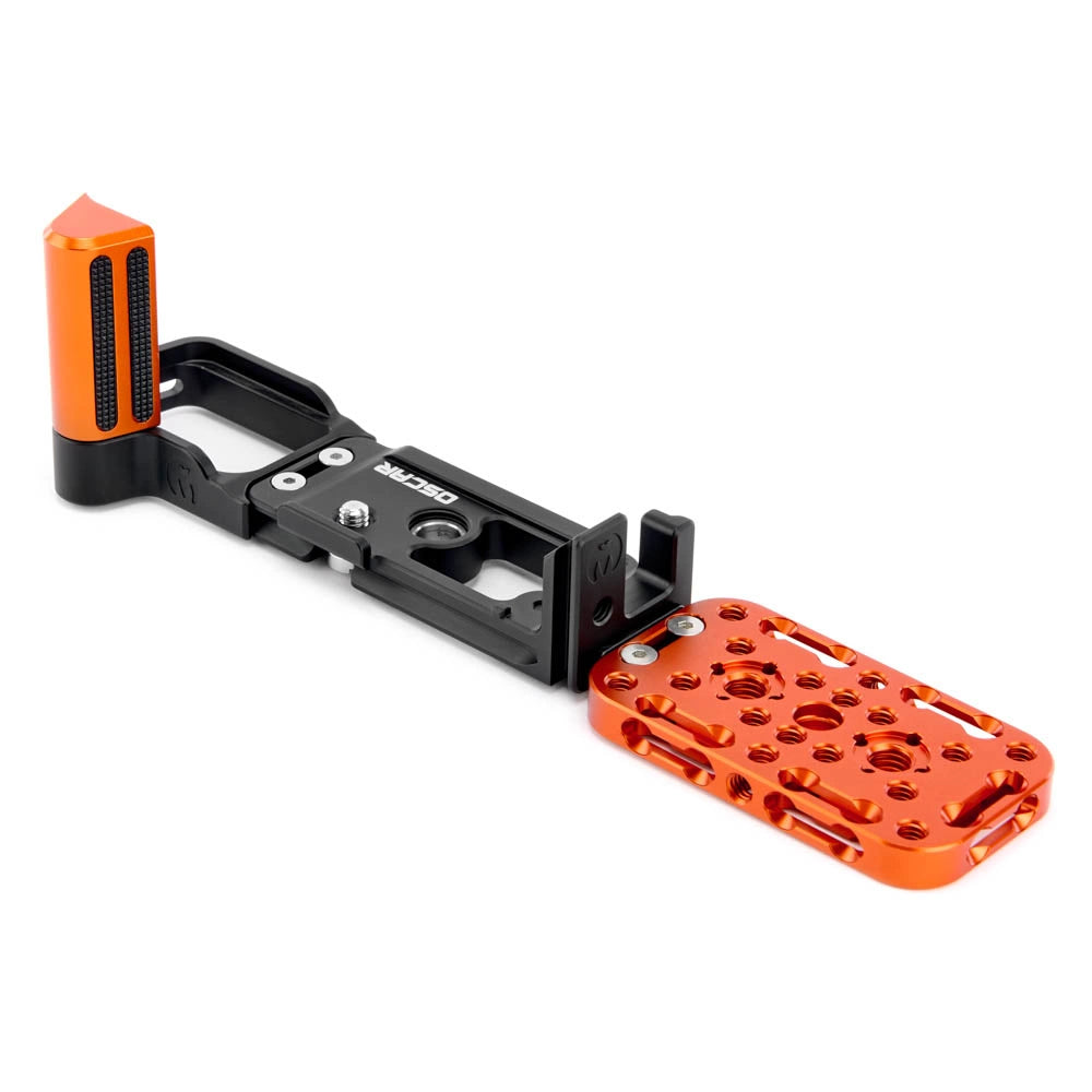 A black metal camera grip extension with bright orange accents, including a textured grip handle and a matching orange footplate, shown on a plain white background.