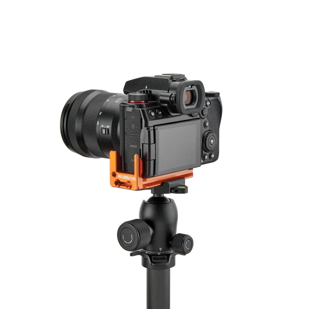 A black camera with a lens attached, mounted on an orange quick-release bracket attached to a black tripod, shown against a solid white background.