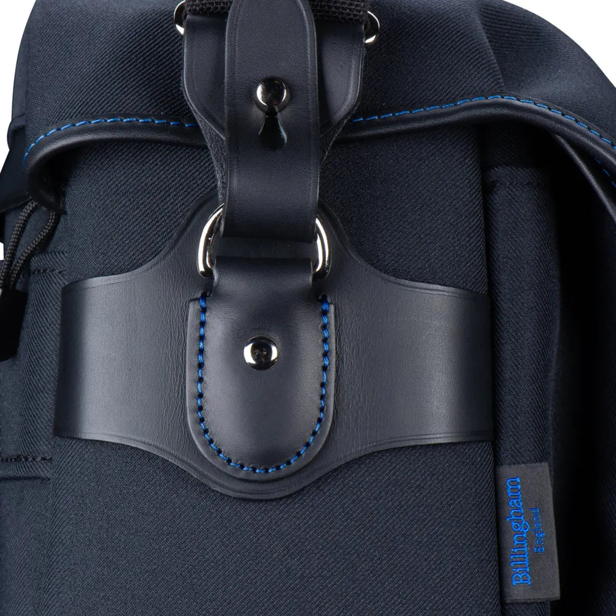 Close-up of a navy backpack with leather strap and brand label on a white background