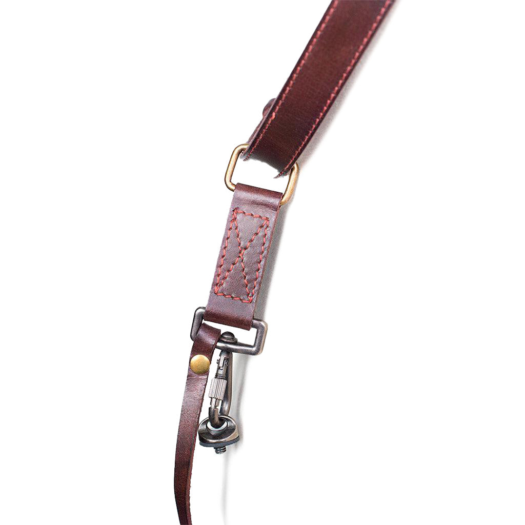 Close-up of a brown leather camera strap with metal hardware on a white background
