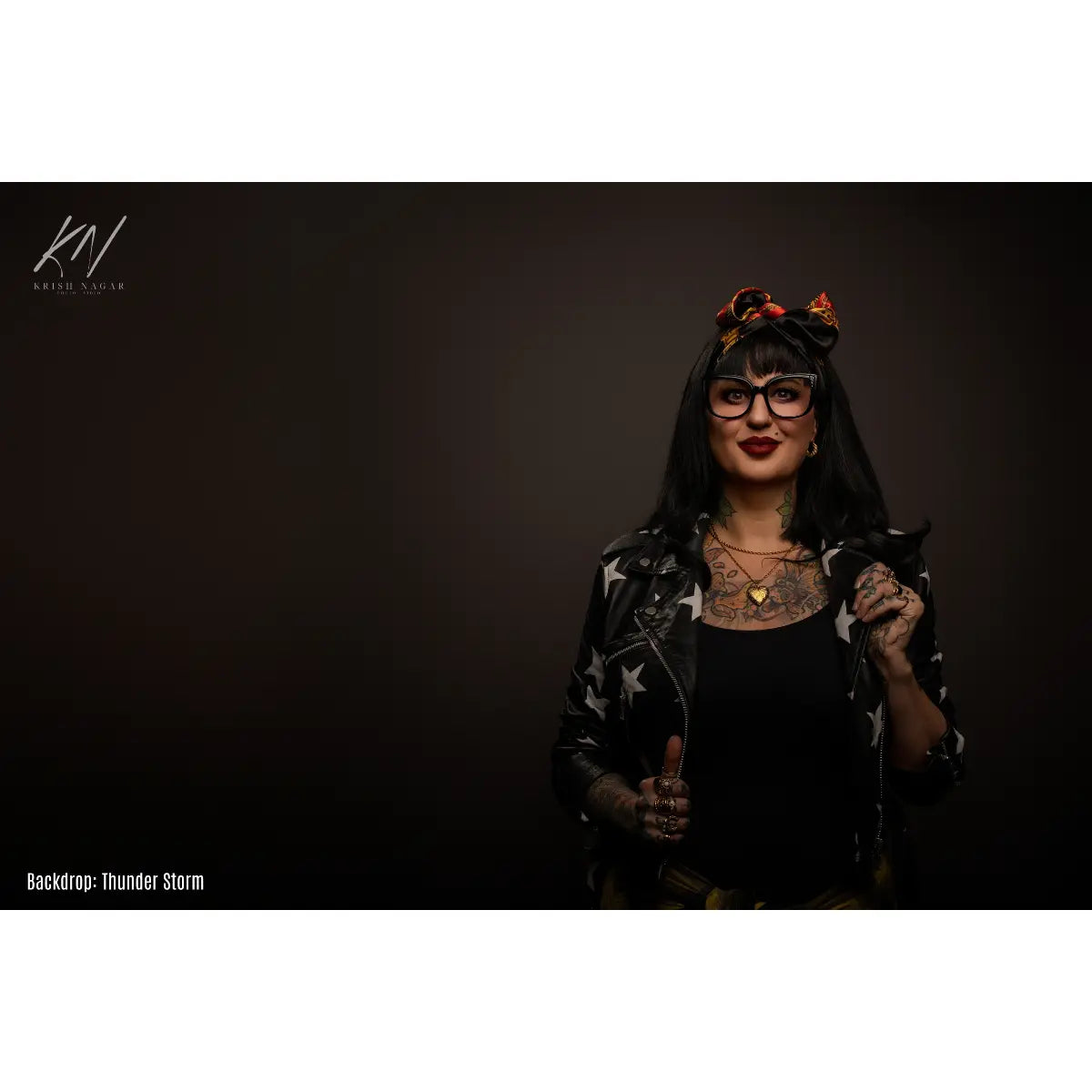 Person with tattoos and glasses holding a microphone against a dark background