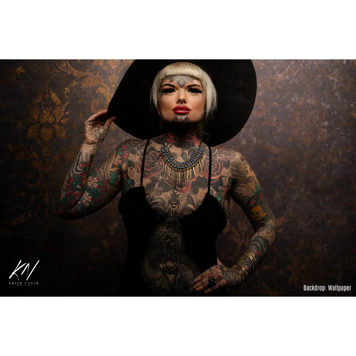 Person with tattoos wearing a black hat against a textured brown background