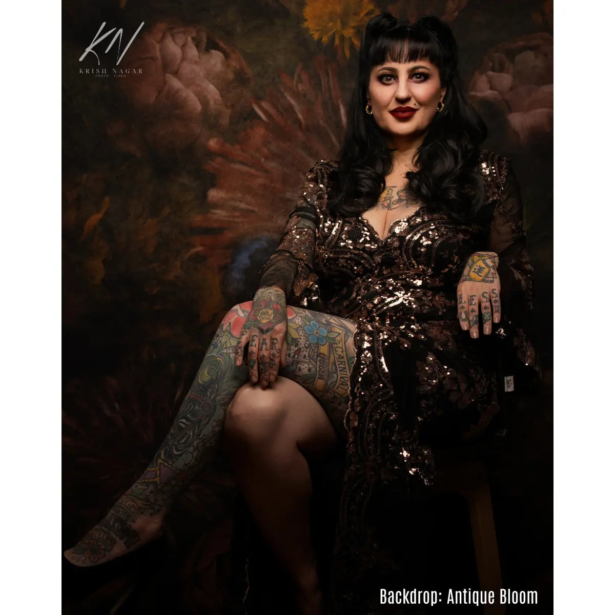 Woman in a glittery dress with tattoos posing against an 'Antique Bloom' backdrop