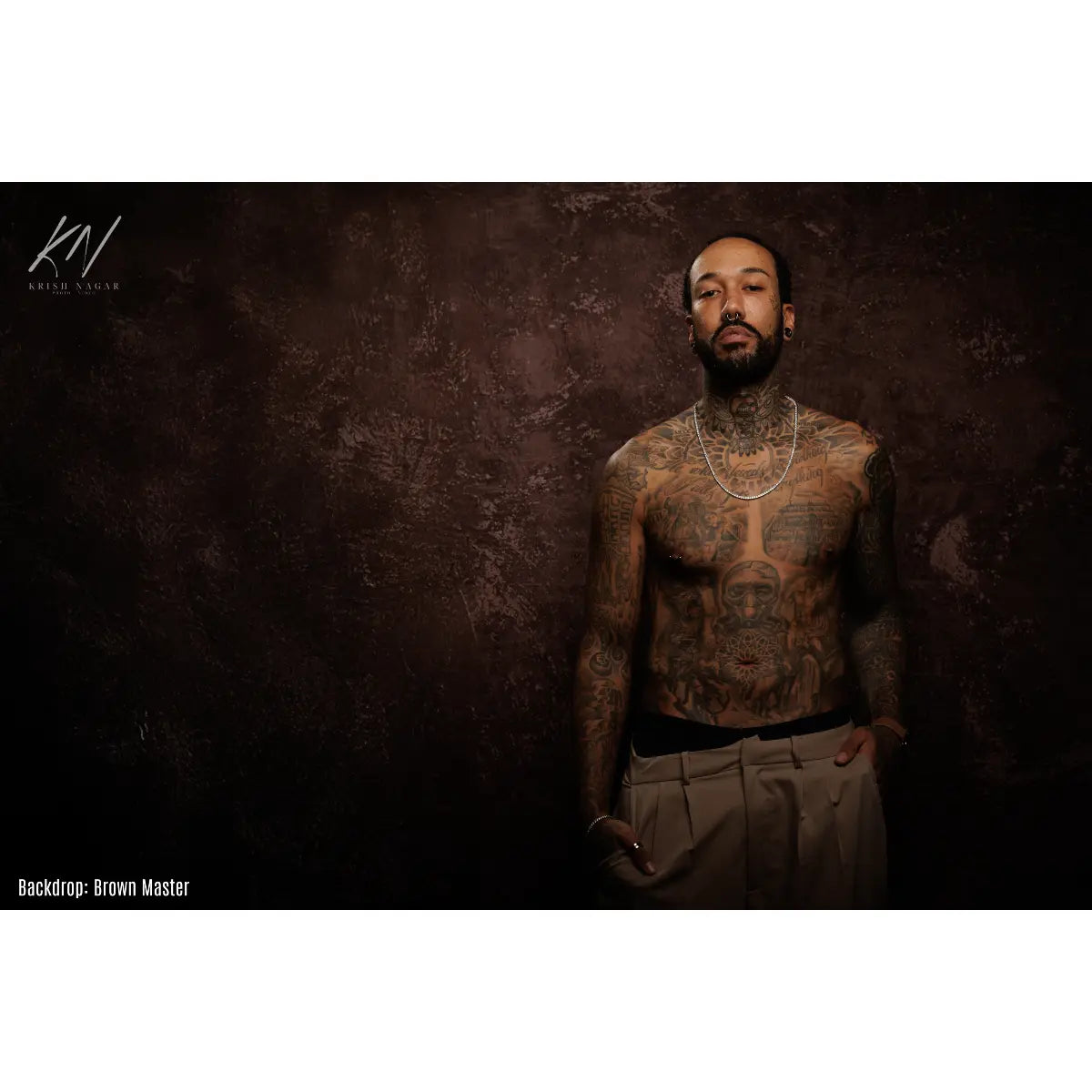 Man with tattoos standing against a textured brown backdrop