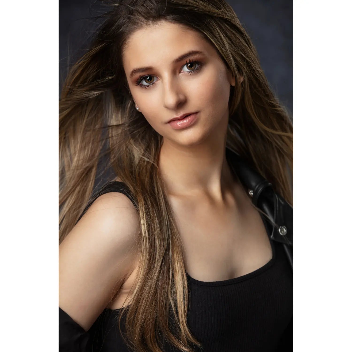 Woman with long brown hair wearing a black top against a dark background