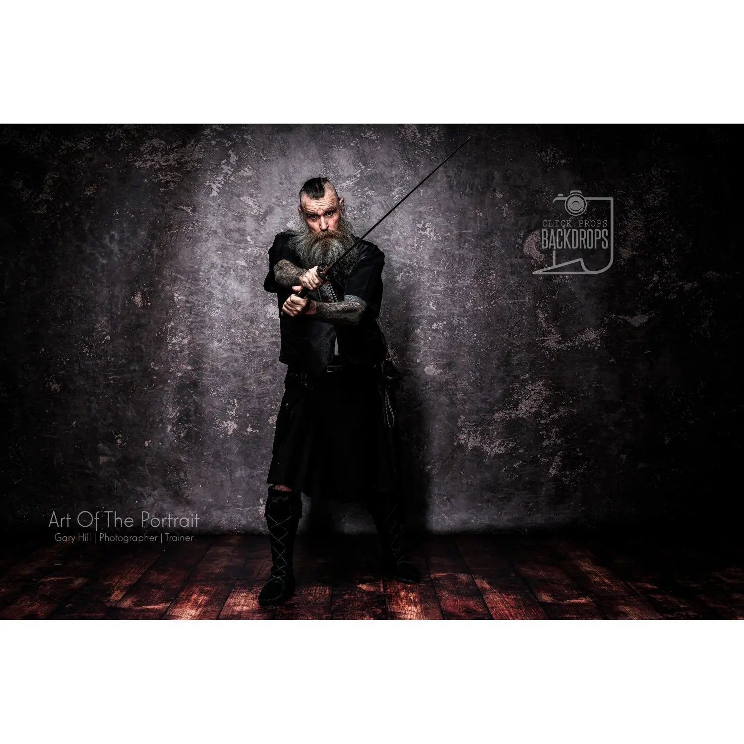 Man in dark clothing holding a sword against a textured dark wall with 'Blue Sky Backdrops' logo.