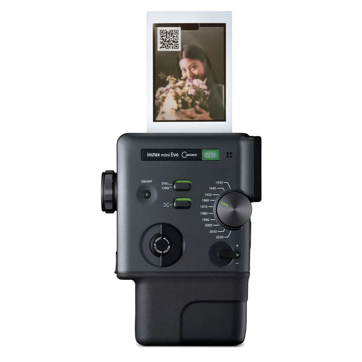 A black Instax Mini Evo Camera with an attached battery grip, shown from the front against a white background. A printed instant photo is emerging from the top slot, and the camera body features green and white controls and branding.