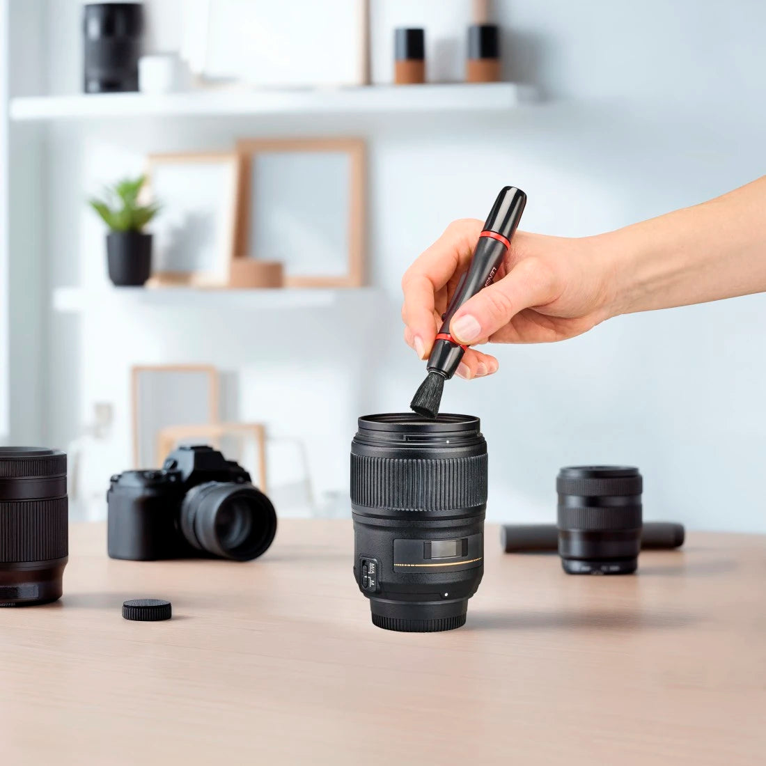 Camera lens being used as a mug with a hand holding a pen over it, surrounded by camera equipment.