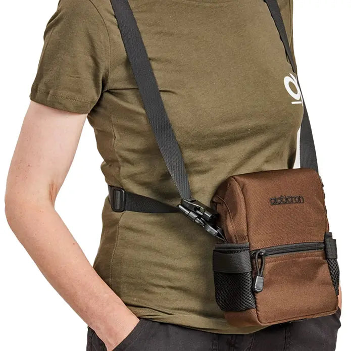 Person wearing a brown crossbody bag over an olive green shirt on a white background