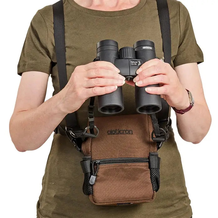 Person holding binoculars with a backpack and camera strap on a white background