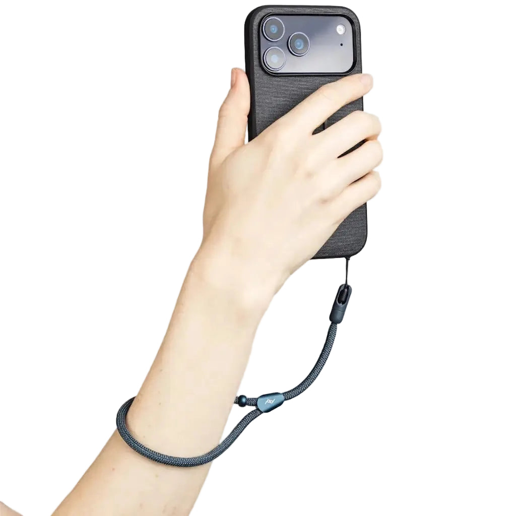 A hand holding a smartphone with a black textured case and a dark gray braided wrist strap attached near the camera cutout, shown against a light gray background.