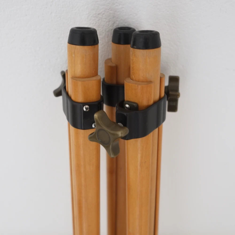 Close-up of a tripod with three wooden legs, black metal locking bands, and a star-shaped adjustment knob against a plain white wall.