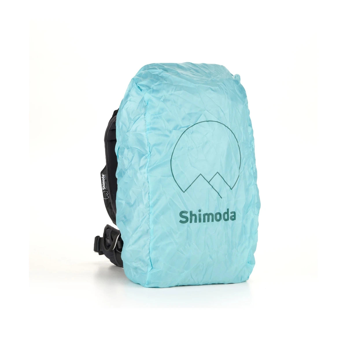 A light blue crinkled waterproof backpack cover with a dark green Shimoda logo and mountain graphic, shown on a white background.