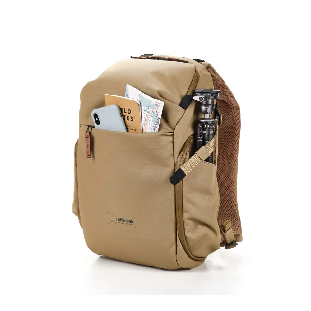 Tan backpack with items like a phone and map on a white background