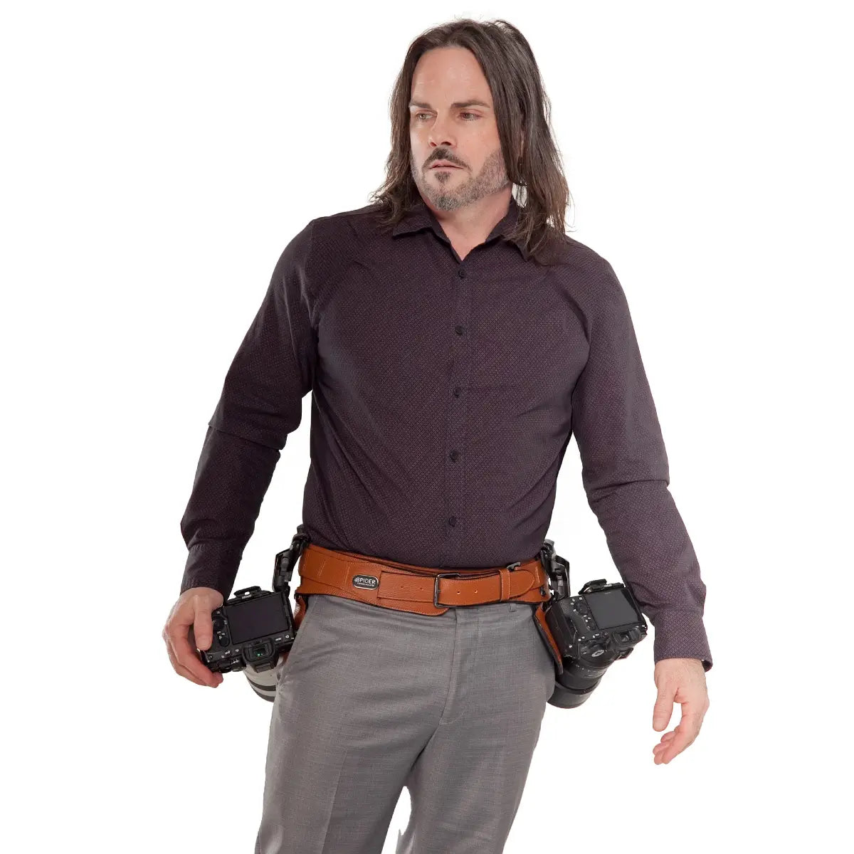 Man wearing a brown shirt and gray pants with a leather belt, holding two cameras.