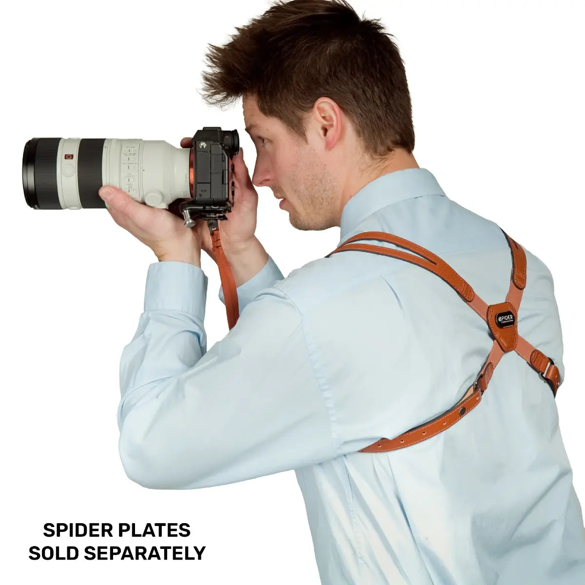 Man holding a camera with a long lens, wearing a leather camera strap, on a white background.