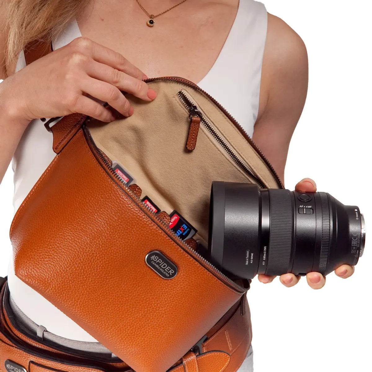 Person holding a brown leather camera bag with a camera lens inside, on a white background.